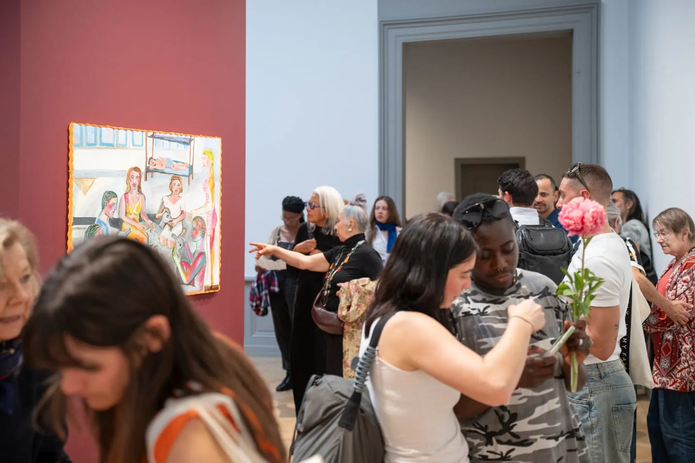Public du vernissage devant une peinture accrochée sur une cimaise rouge bordeaux