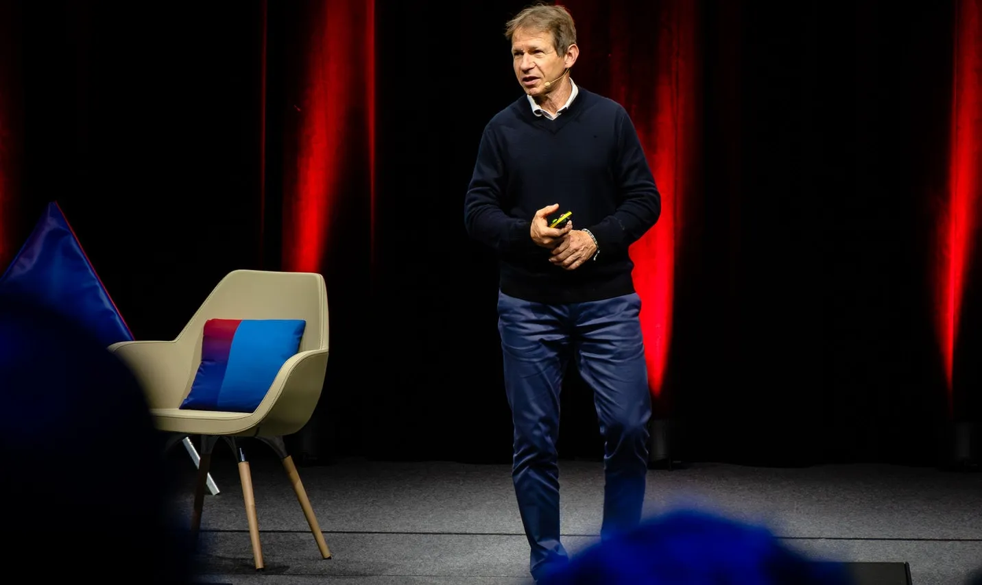 Speaker on stage beside a blue and red triangle and an armchair