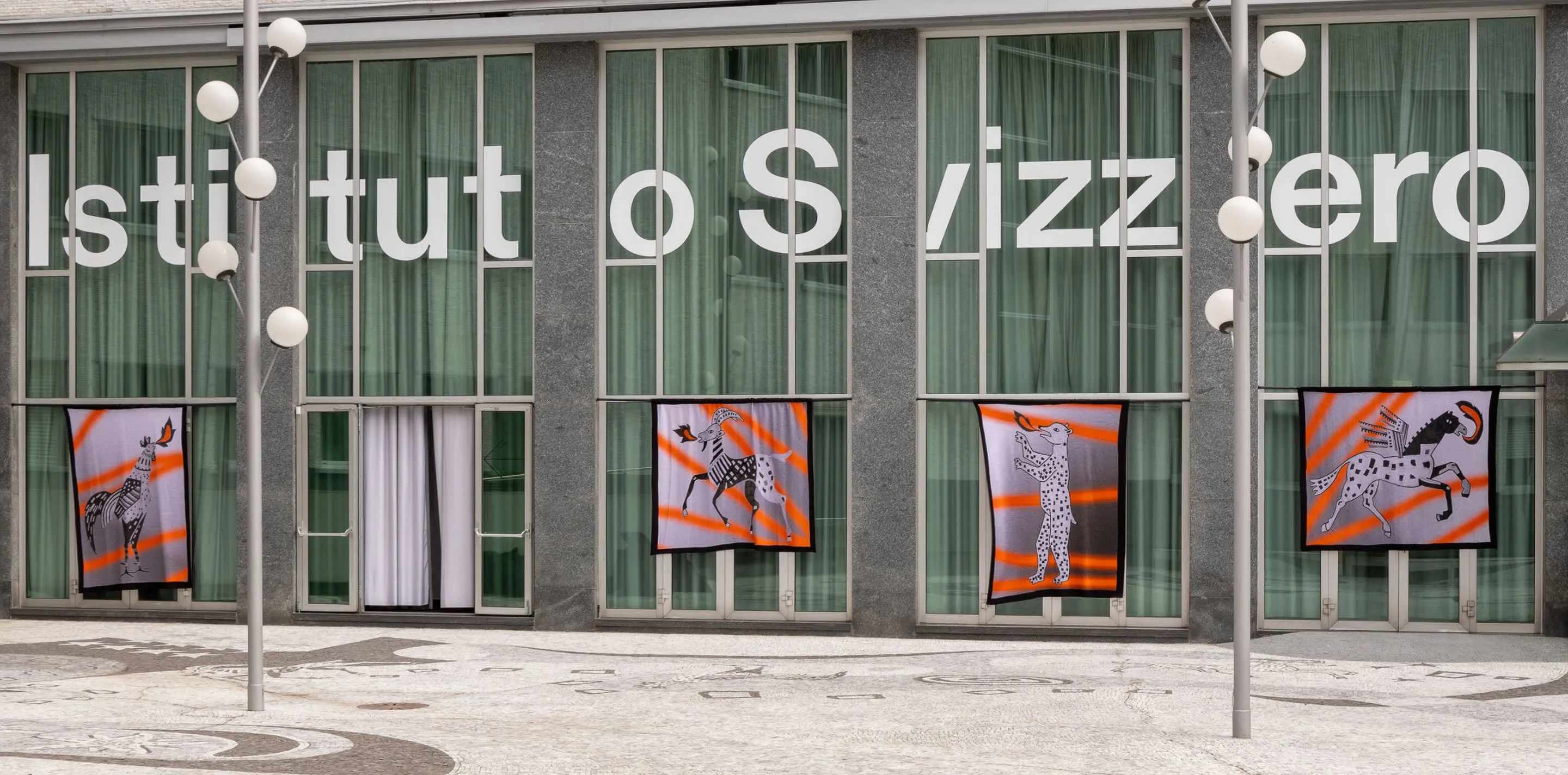 Couvertures Pisoni–lab illustrées d'animaux, suspendues devant la façade vitrée de l'Istituto Svizzero, Milan