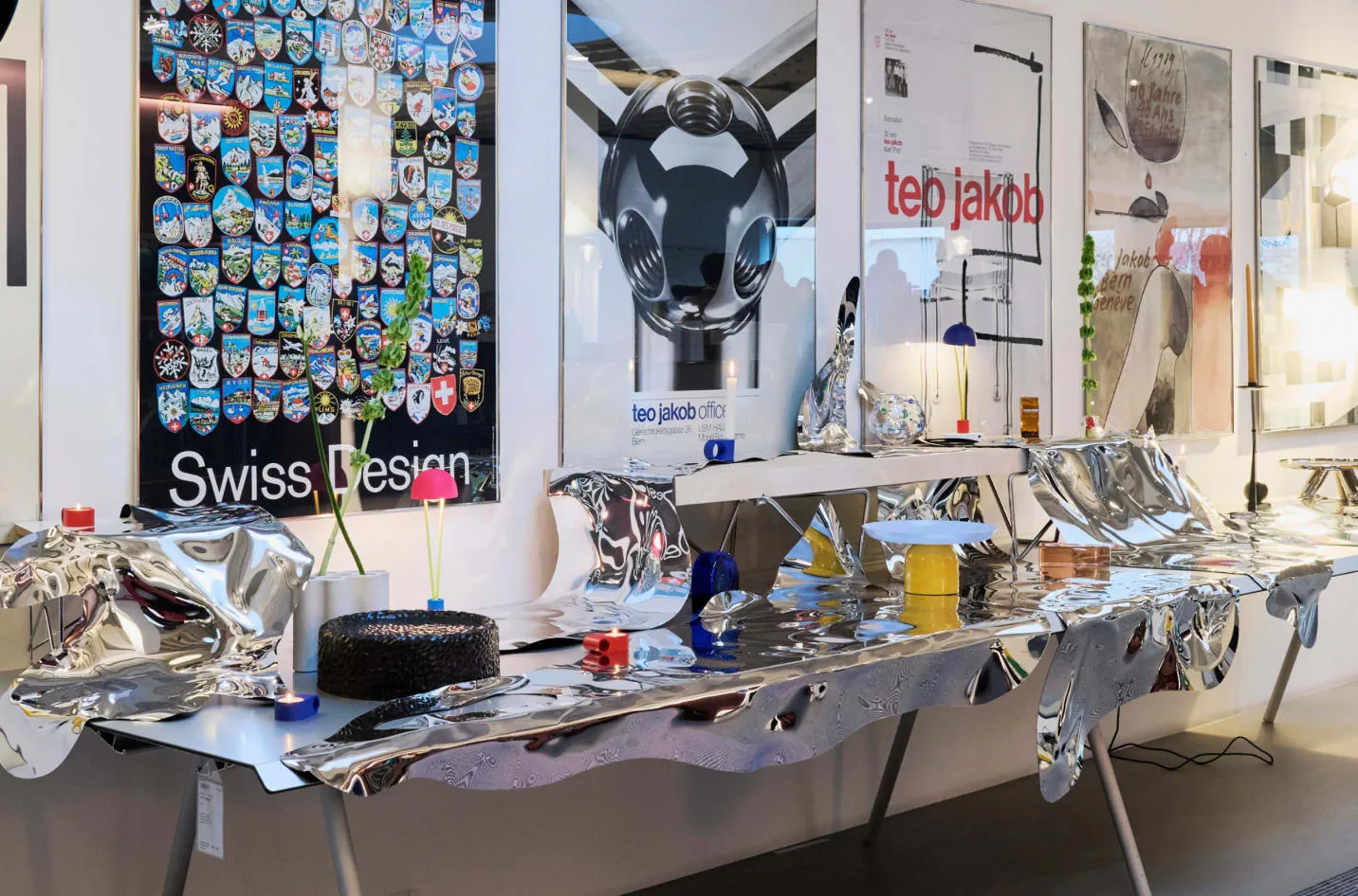 Table recouverte de surfaces miroir thermoformées Pisoni–lab devant les affiches du showroom Teo Jakob