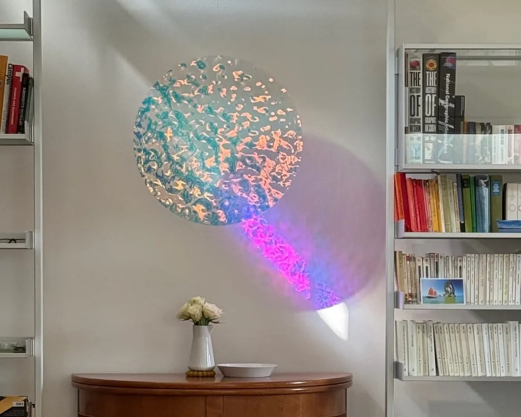 Disque Sparkle Pisoni–lab suspendu dans un salon, reflets bleus, orange et rose au mur