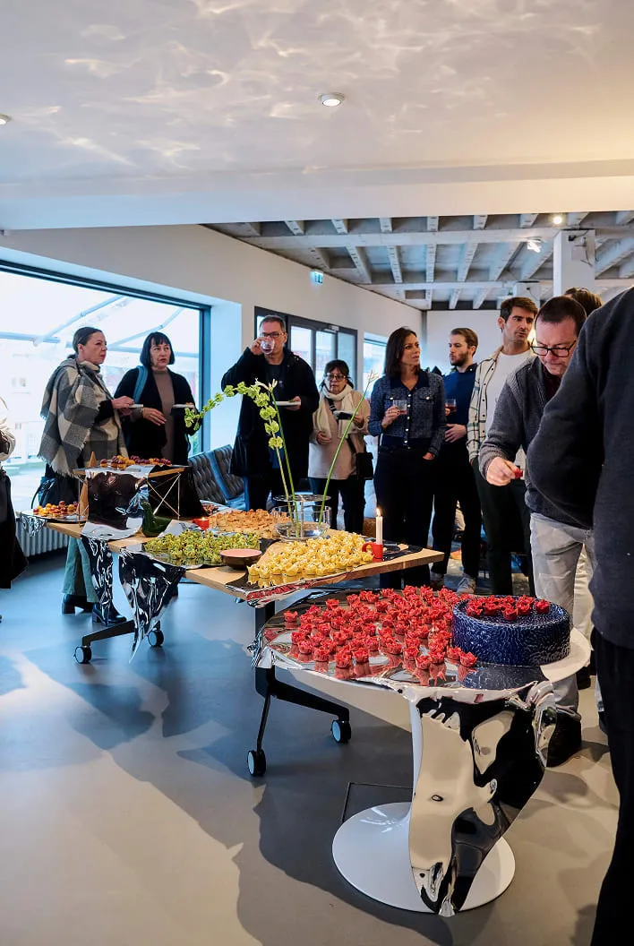 Invité·e·s autour du buffet, tartelettes rouges sur un pied de table habillé de miroir