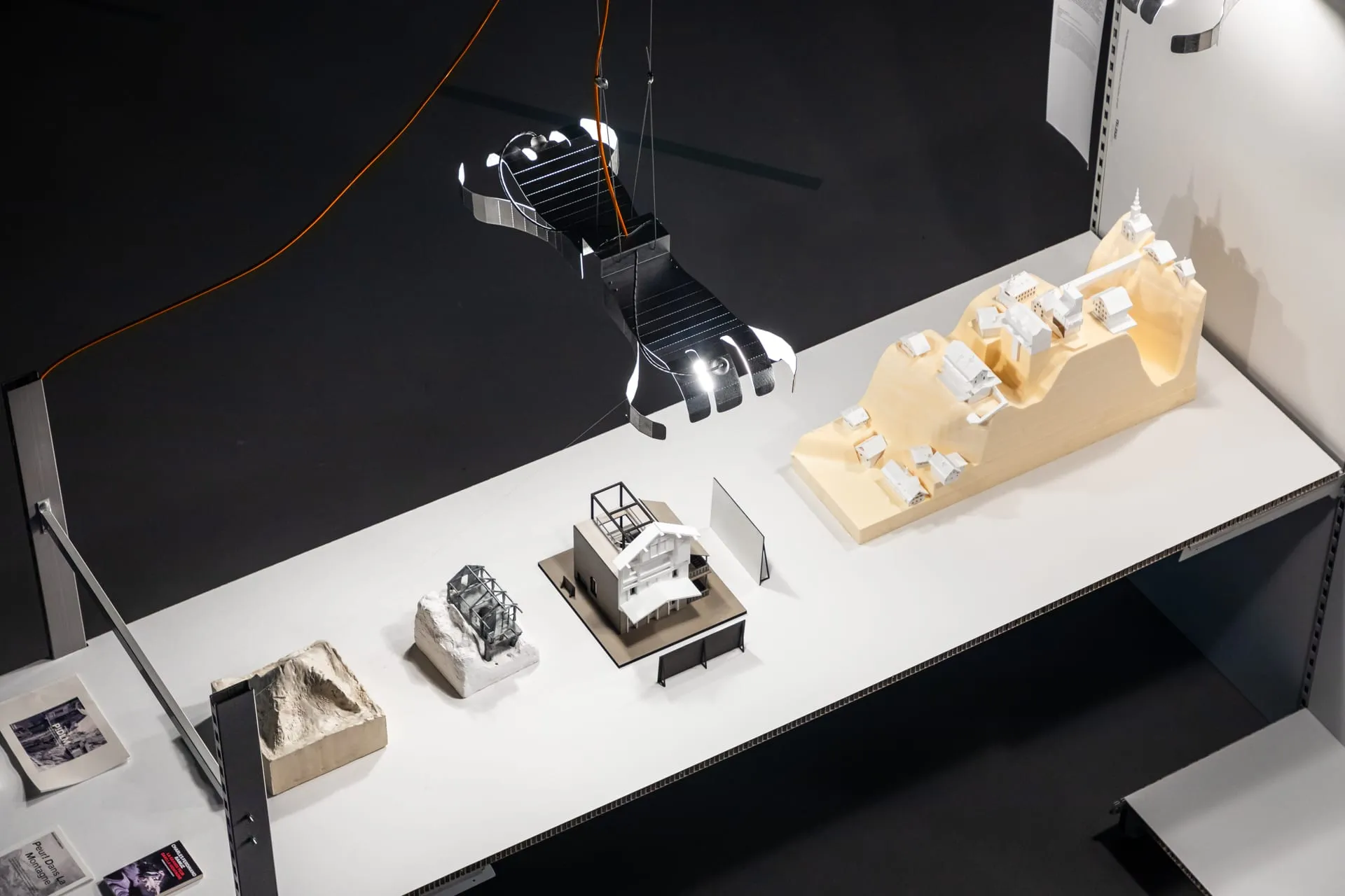 Plusieurs maquettes d'architecture sur un longue table illuminé par une lampe Pisoni-lab