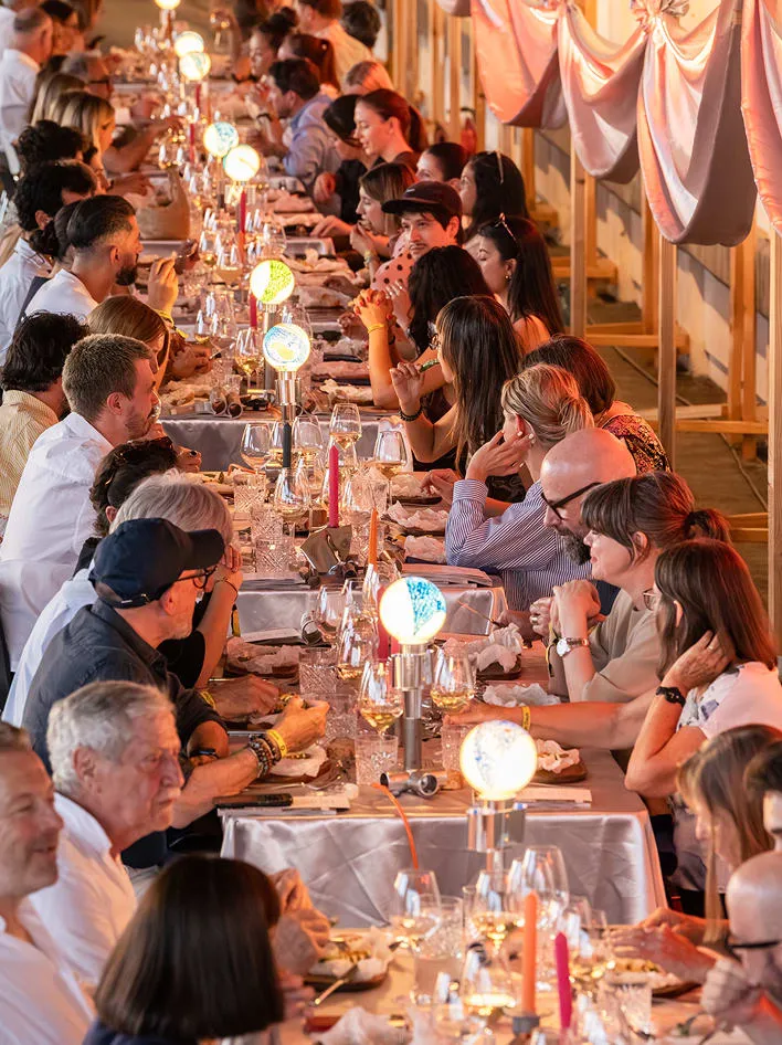 Convives le long de la table, lampes Pisoni–lab et drapés roses au plafond