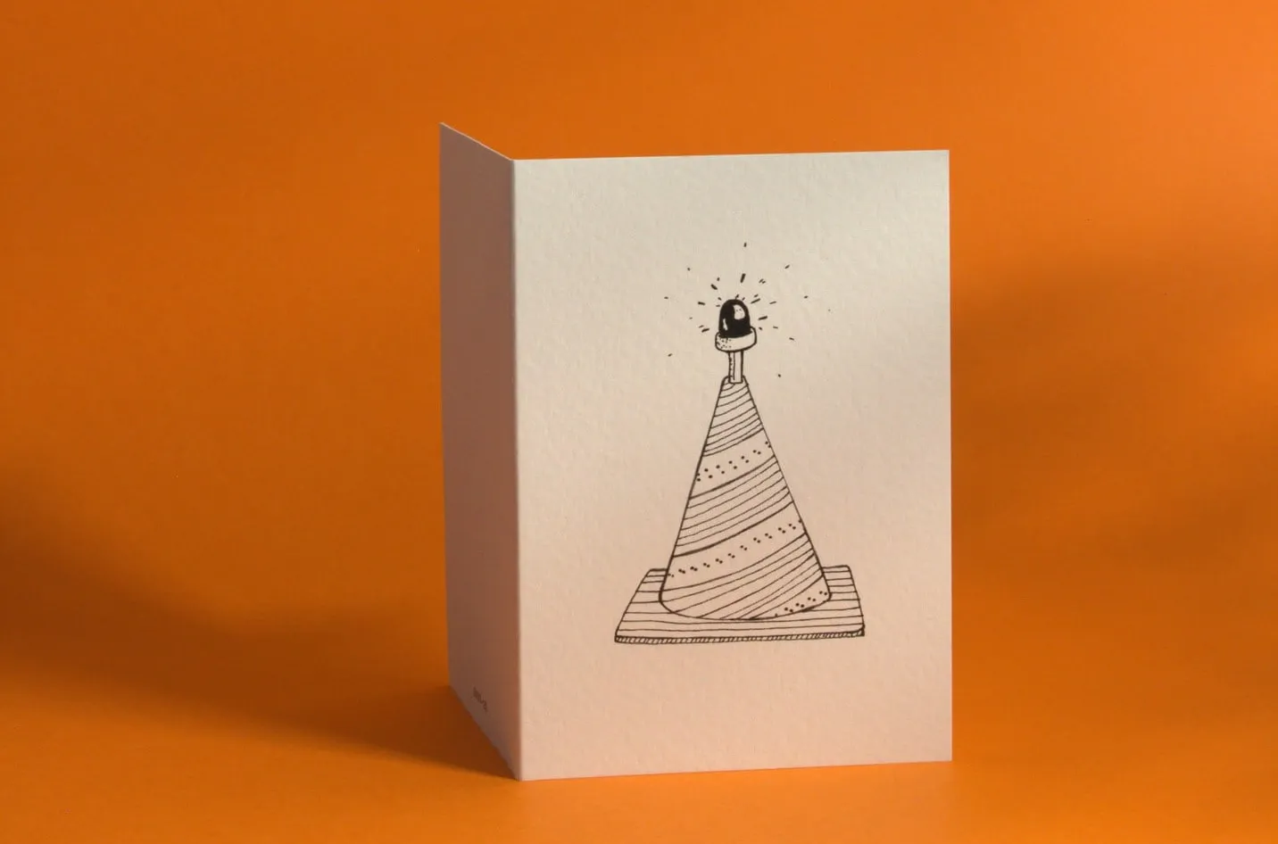 Carte illustrée d'un cône dessiné à l'encre, posée sur un fond orange